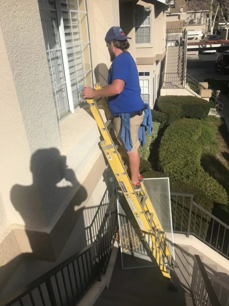 Alan's Cleaning technician on a ladder washing second-story windows of a Laguna Hills home