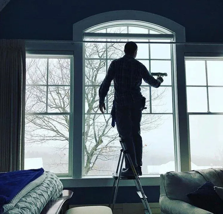 Alan's Cleaning technician squeegeeing tall arched living-room windows from a stepladder